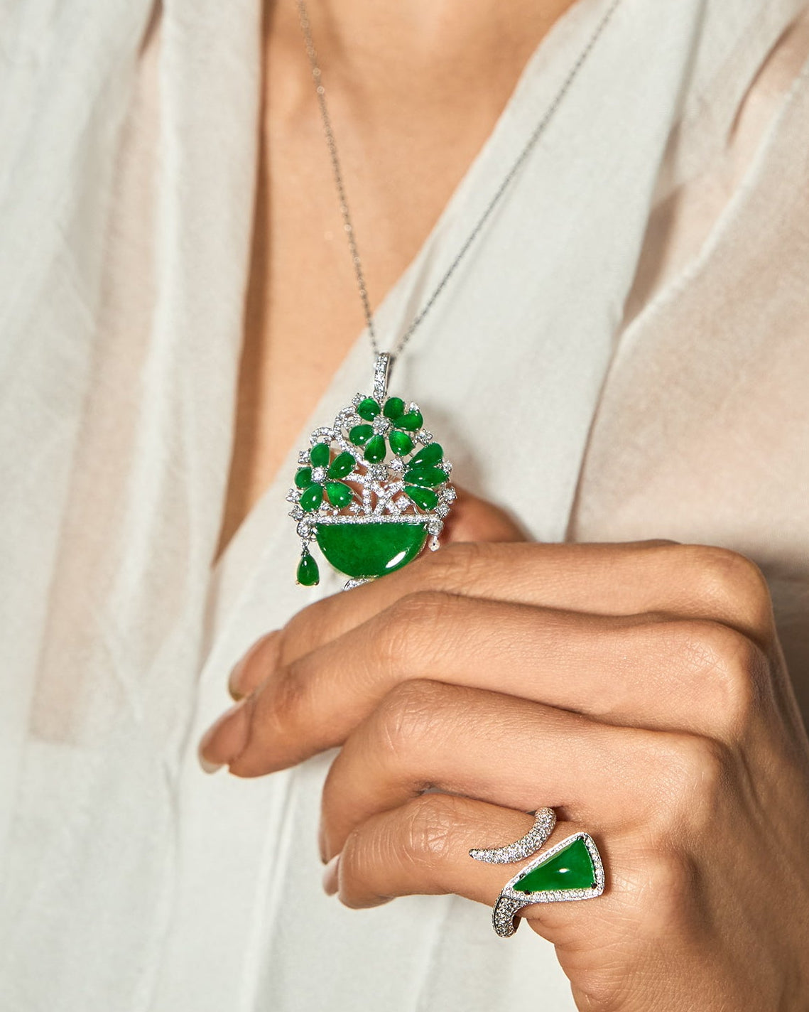 Editorial portrait of model wearing a silk top, one hand gently holding The Floral Pendant at the front and The Orbit Ring — Triangular Bypass worn on the pinky finger.