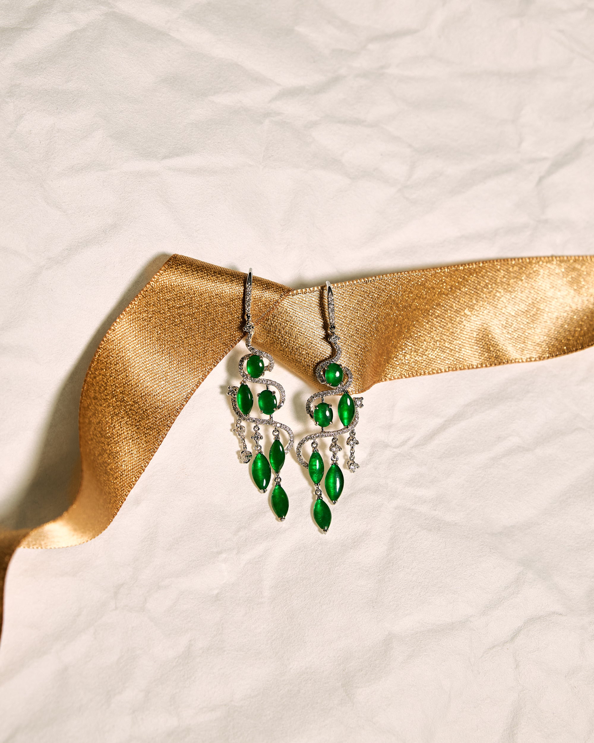Bright green jadeite drop earrings with pavé diamond cascade, front view showing tiered oval and marquise cabochons, set against a white background accented with a gold ribbon, front view.