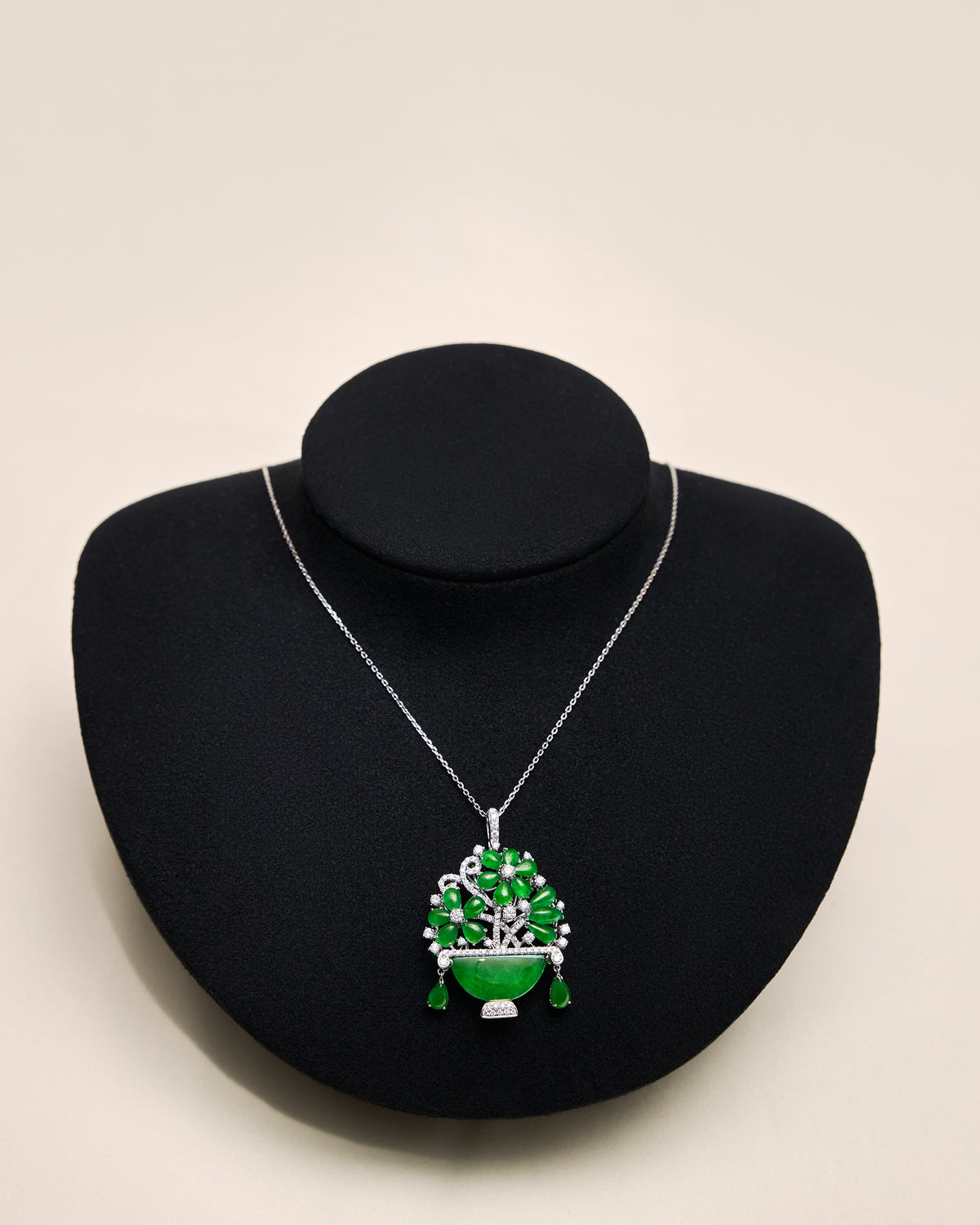 Floral jadeite pendant with oval and pear-shaped cabochons and pavé diamond stems displayed on a black neck bust, front view.