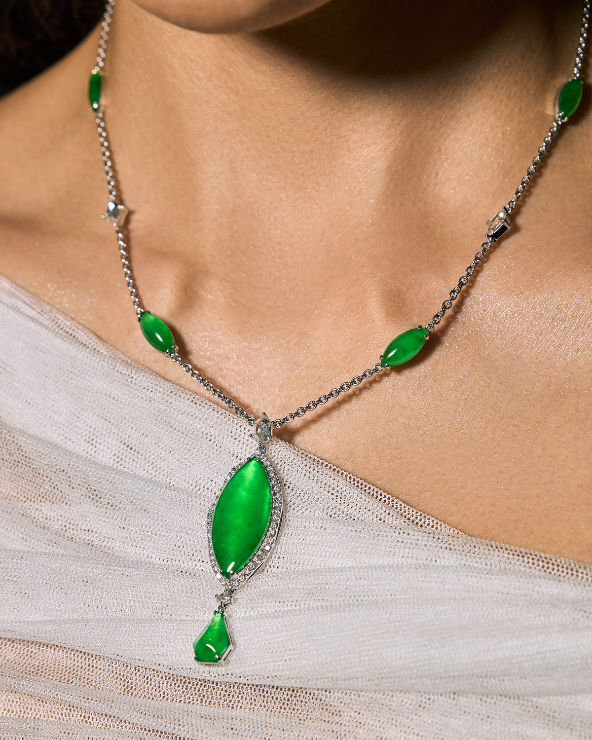 Close-up of The Marquise Cascade Necklace worn on a model, the largest marquise-shaped jadeite cabochon resting on an ivory silk top at the chest while the smaller graduated cabochons and rose-cut diamonds lie against the skin along the collarbone.