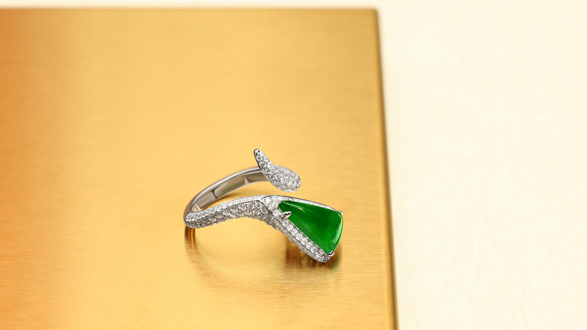 Triangular bright green jadeite bypass ring with pavé diamond band on a gold tray, front view showing triangle-up orientation.