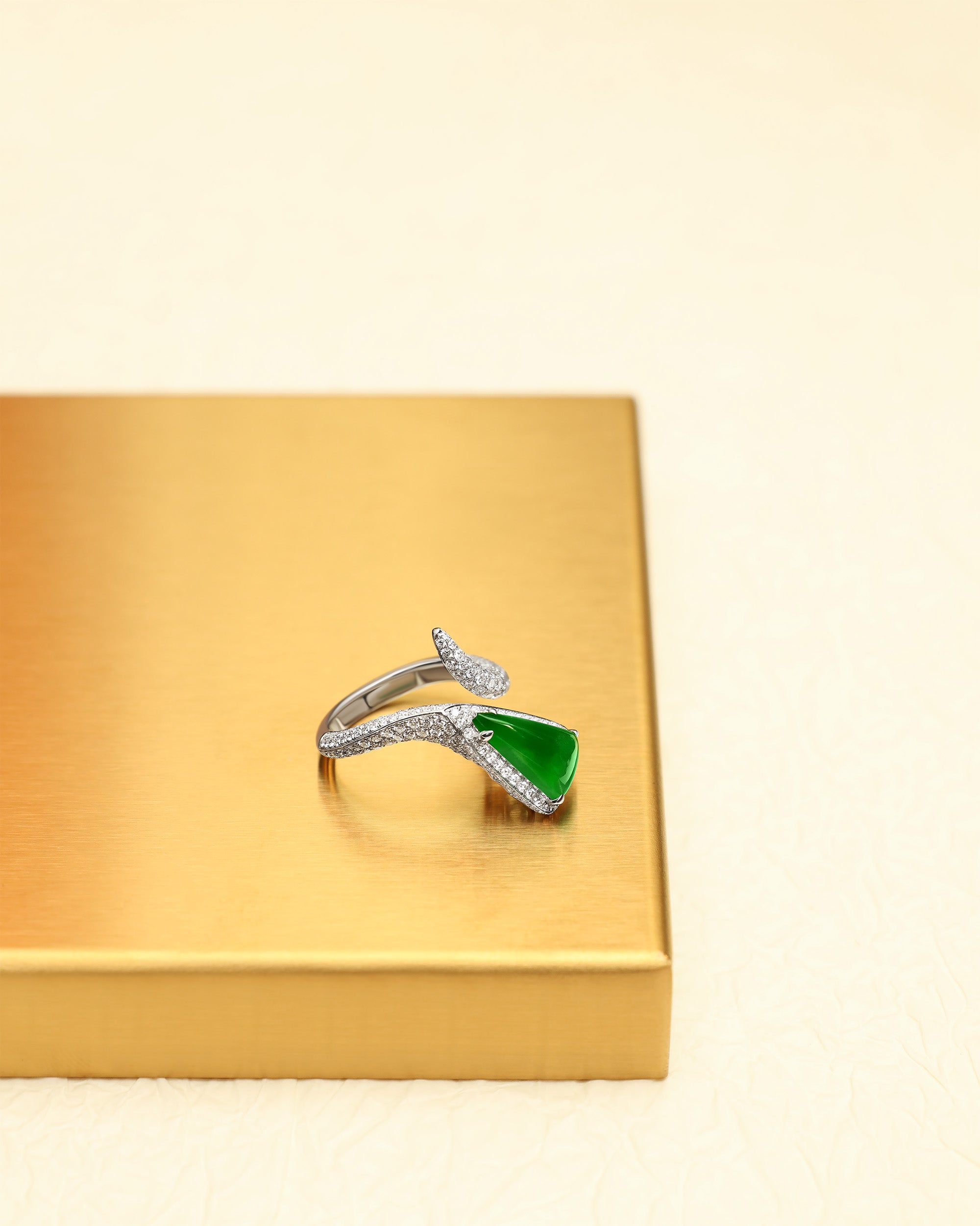Triangular bright green jadeite bypass ring with pavé diamond band on a gold tray, front view showing triangle-up orientation.