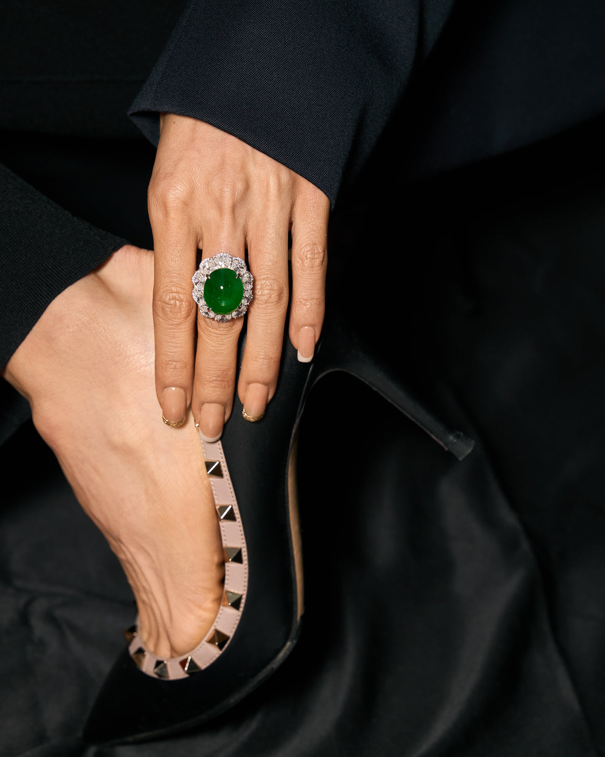 The Oval Cabochon Ring worn on a model's hand resting at her heel, showcasing the intense green oval cabochon framed by ten matched oval diamonds.