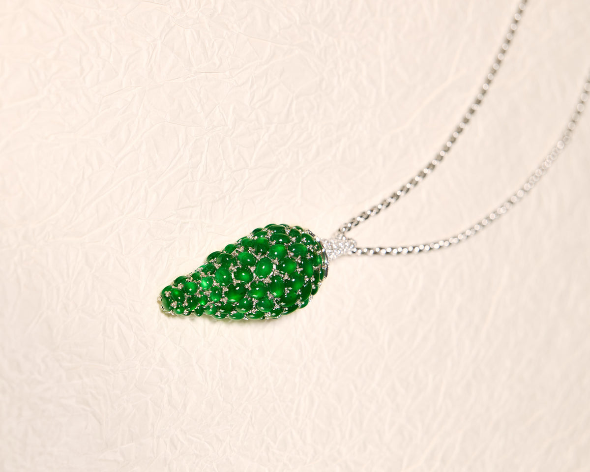 Whimsical pepper motif pendant composed of graduating emerald green oval jadeite cabochons and pavé diamonds on a white background, front view.