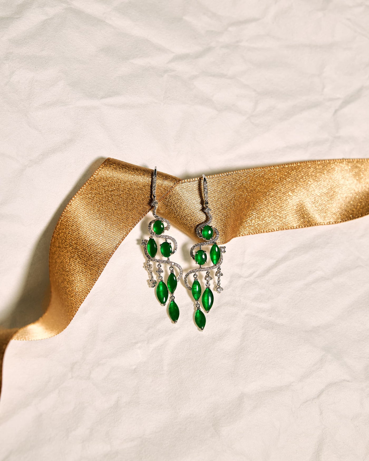 Bright green jadeite drop earrings with pavé diamond cascade, front view showing tiered oval and marquise cabochons, set against a white background accented with a gold ribbon, front view.