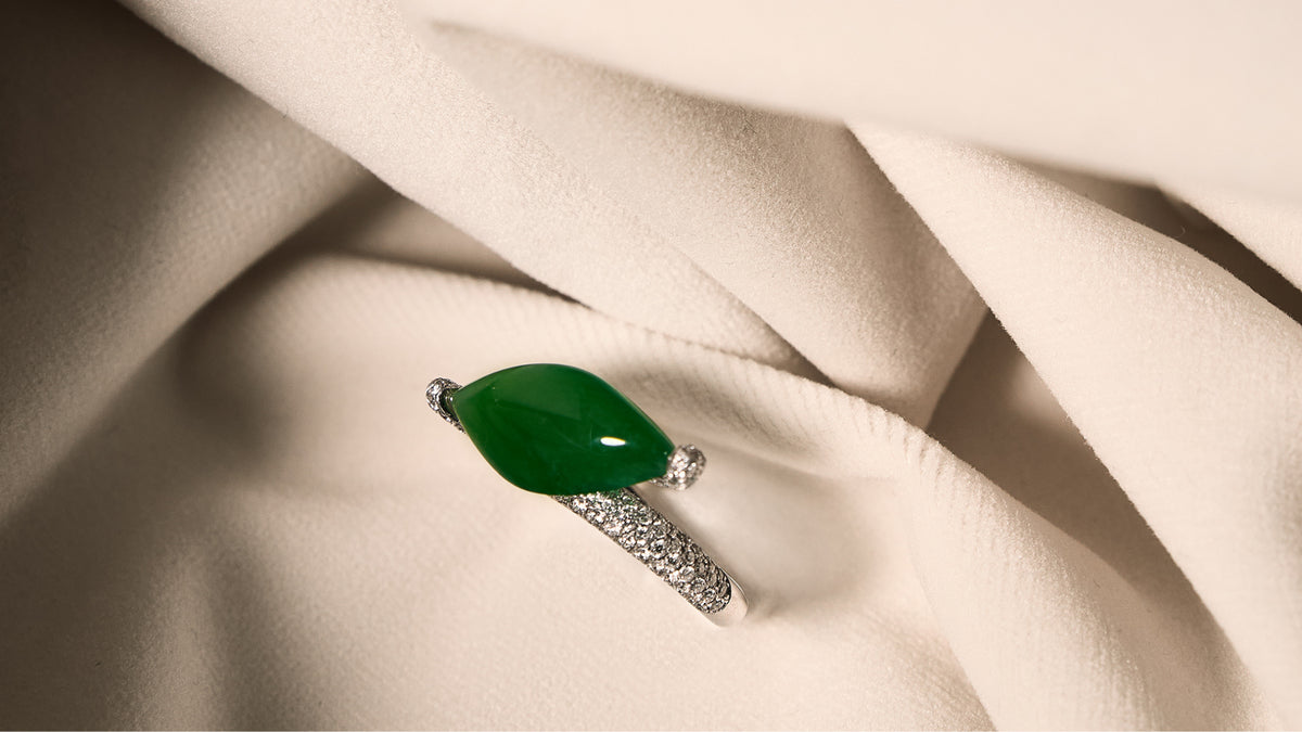 Intense green marquise jadeite ring with east-west bypass pavé diamond band on ivory cloth, front view showing full unobstructed stone face.