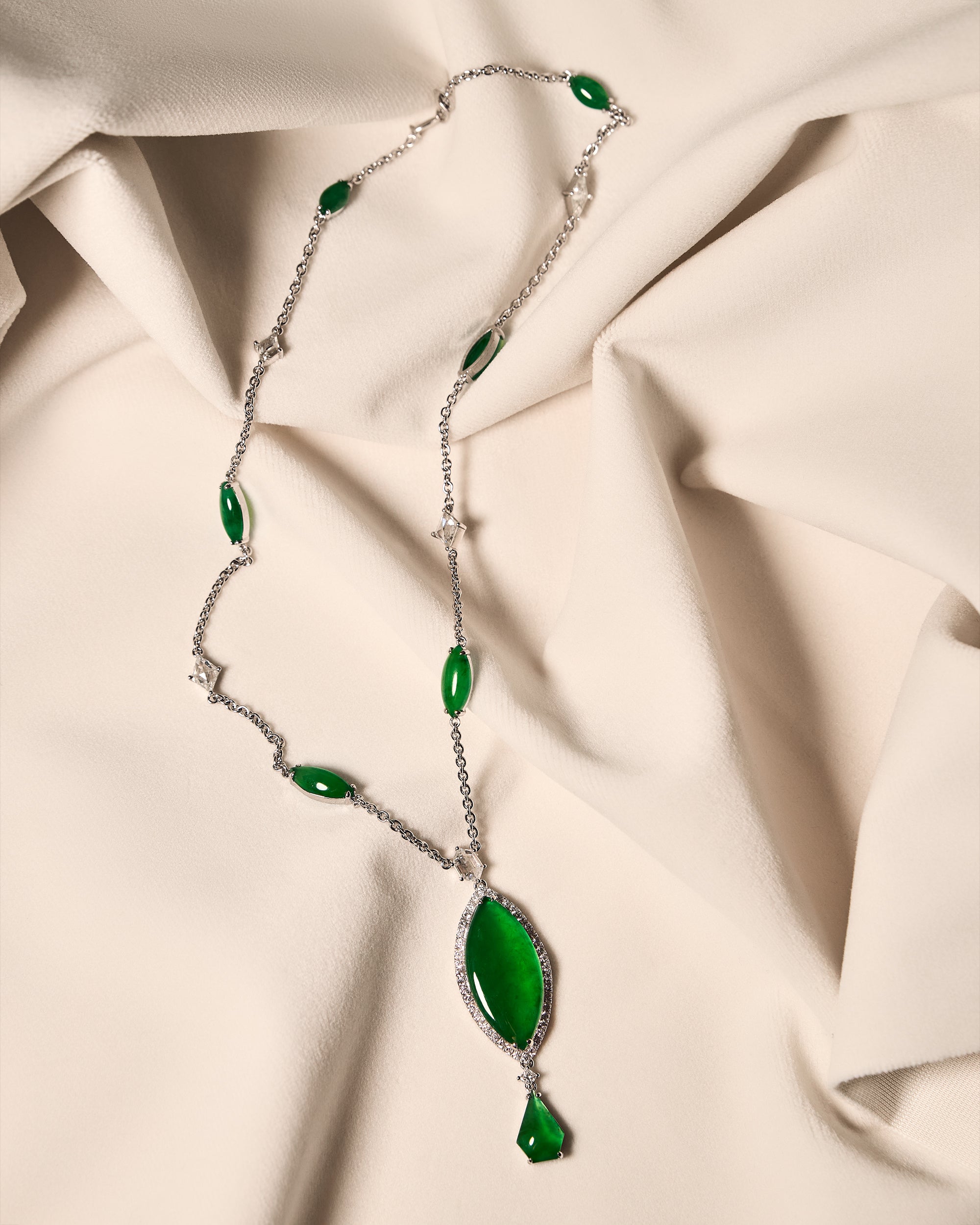Graduated marquise-shaped jadeite cascade necklace alternating with rose-cut diamonds on an ivory cloth, front view showing the full pendant assembly.