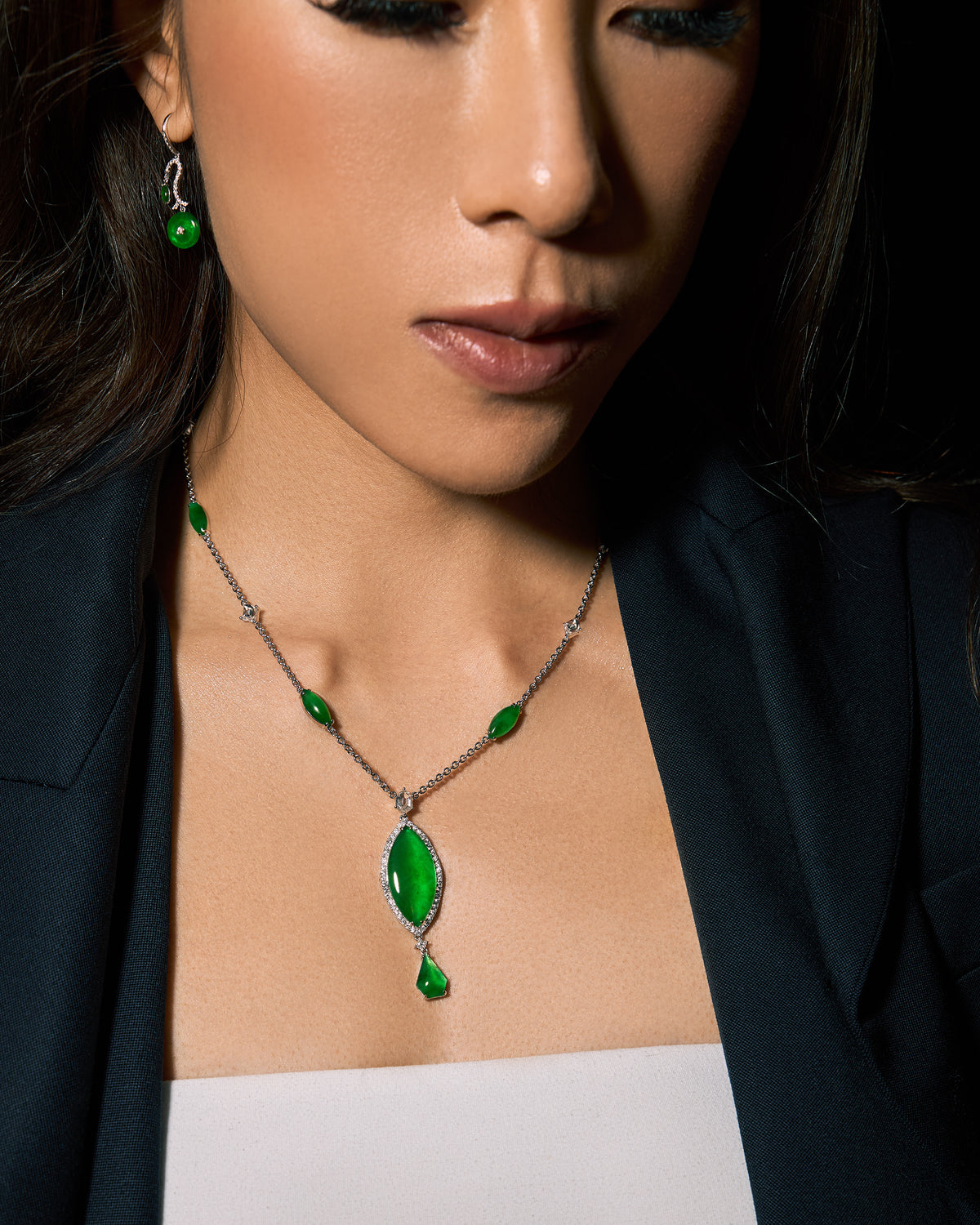 The Marquise Cascade Necklace worn on a model in a black blazer, highlighting the 48mm pendant drop and graceful drape of the graduated jadeite cabochons along the collarbone, styled with The Arc & Marquise Drop Earrings.