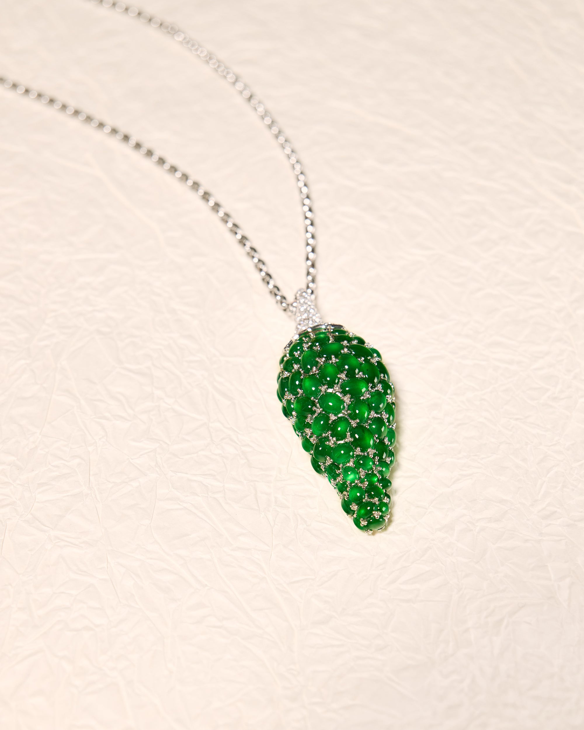 Whimsical pepper motif pendant composed of graduating emerald green oval jadeite cabochons and pavé diamonds on a white background, front view.