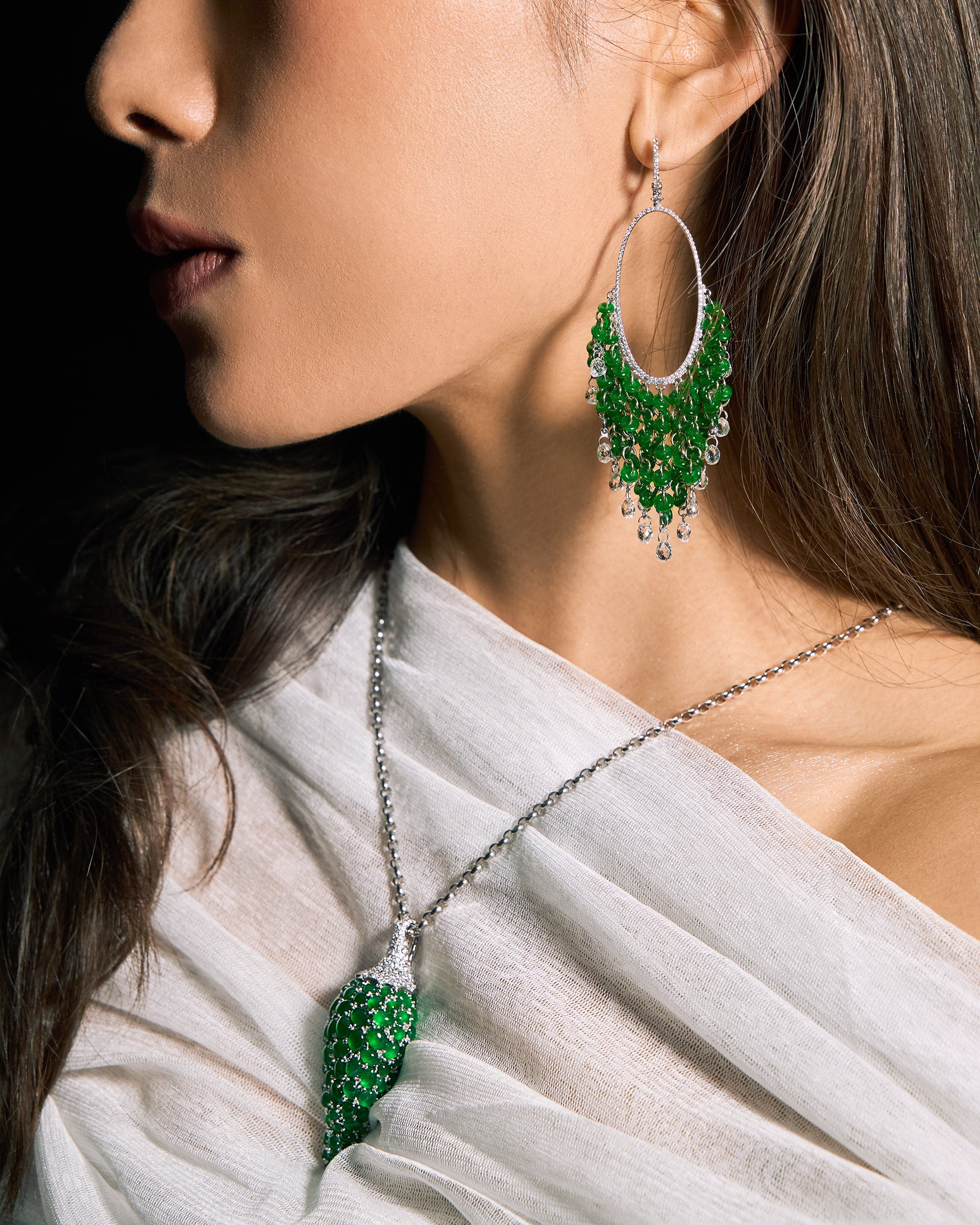 The Pepper Motif Pendant worn on a model in an ivory silk top in side profile, showcasing the sculptural volume of the graduating jadeite stones and the continuous pavé diamond stem, styled with The Fringe Disc Drop Earrings.
