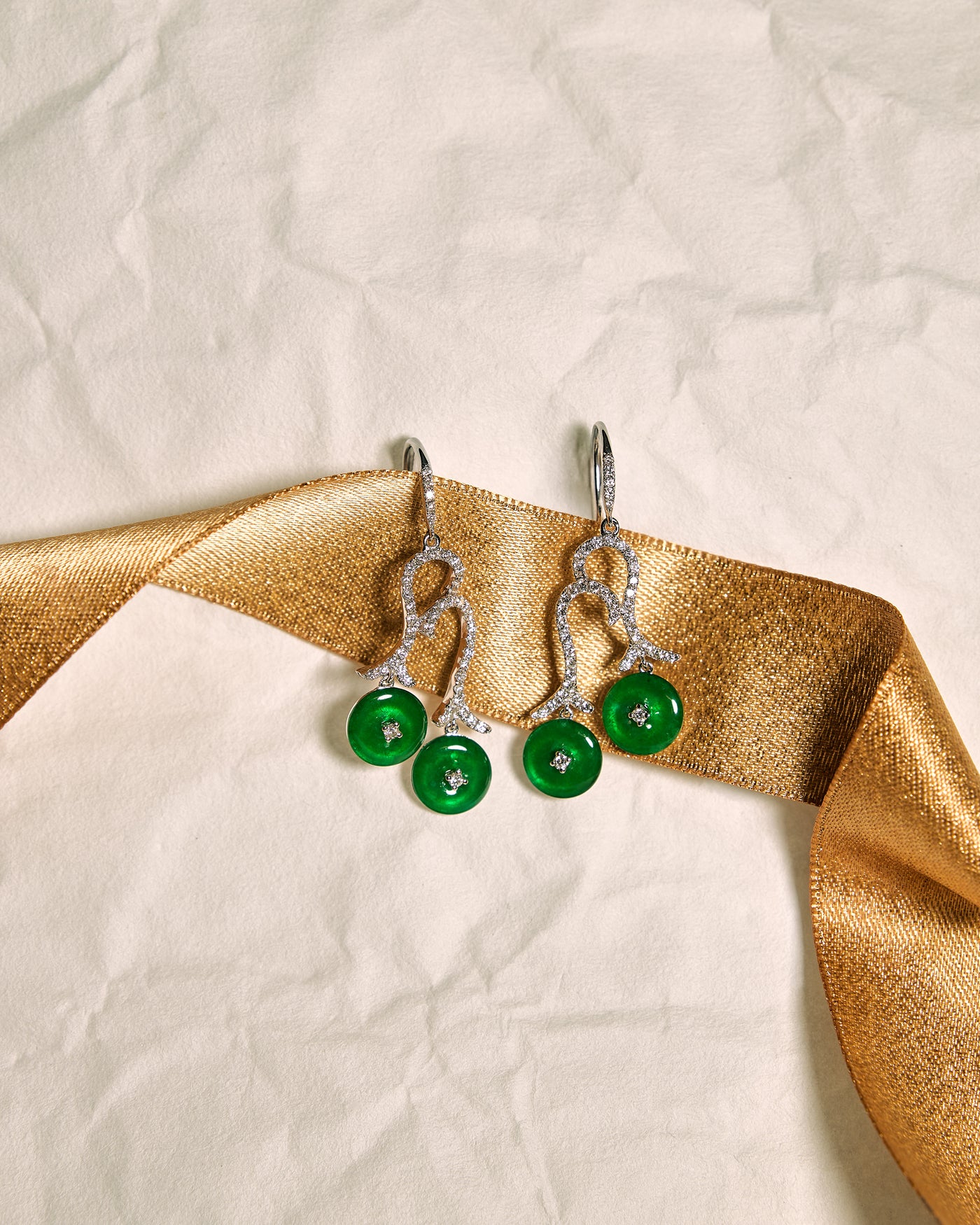 Twin Arc Drop Earrings featuring pavé diamond arcs and flat huaigu jadeite discs, highlighting elegant curves, set against a white background accented with a gold ribbon, front view.